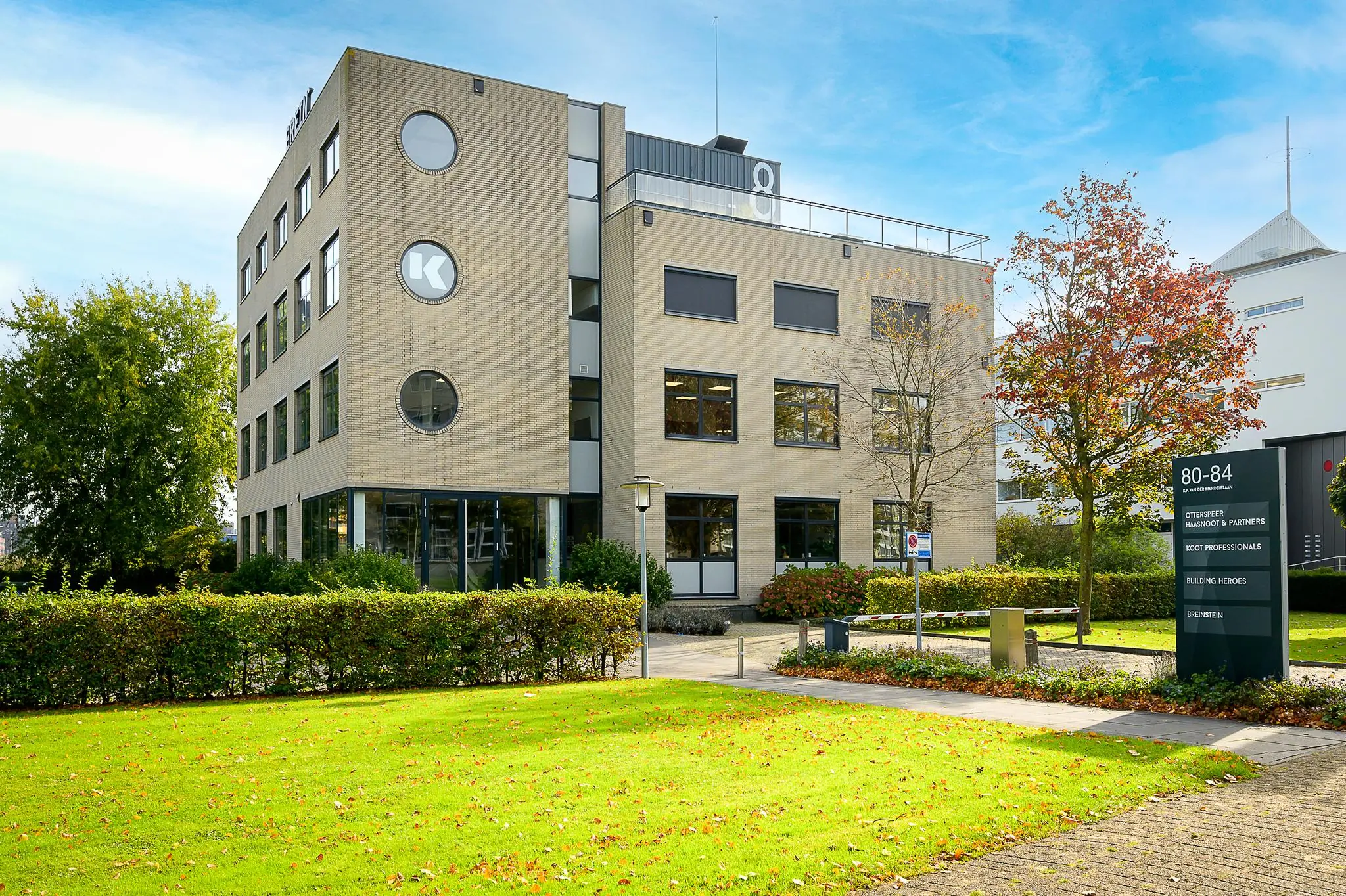 Kantoorgebouw aan de K.P. van der Mandelelaan 80-84 in Rotterdam met bedrijfsnamen op een bord in de voortuin.